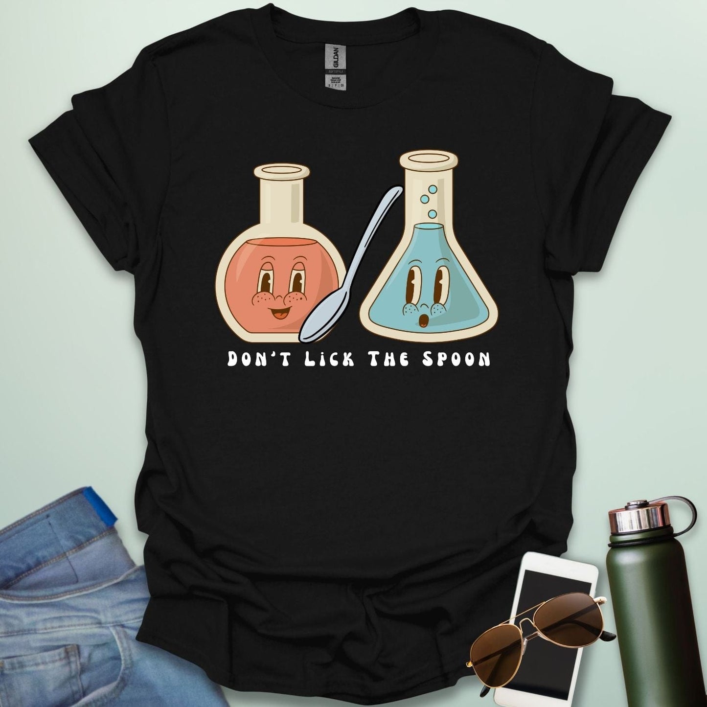 A black t-shirt with a cartoon illustration of two lab flasks and a spoon, with the text 'Don't Lick The Spoon.