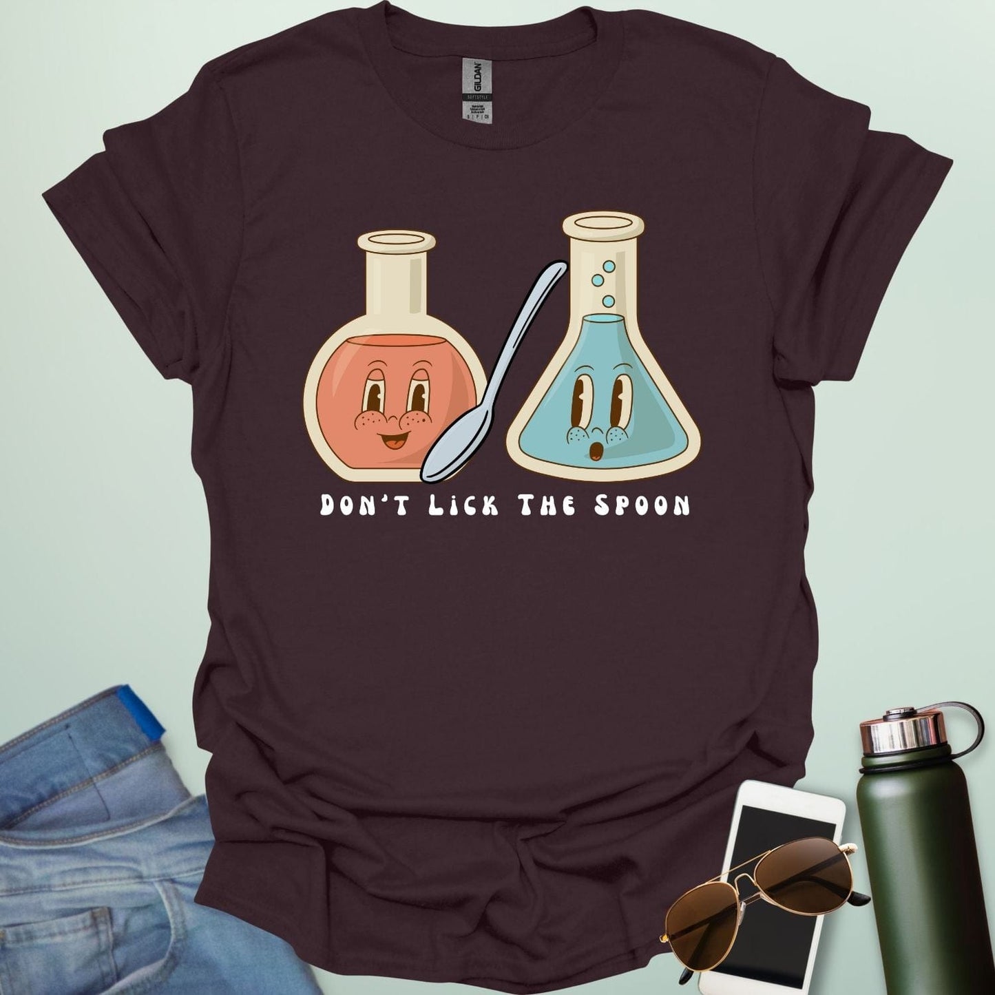 A dark chocolate t-shirt with a cartoon illustration of two lab flasks and a spoon, with the text 'Don't Lick The Spoon.