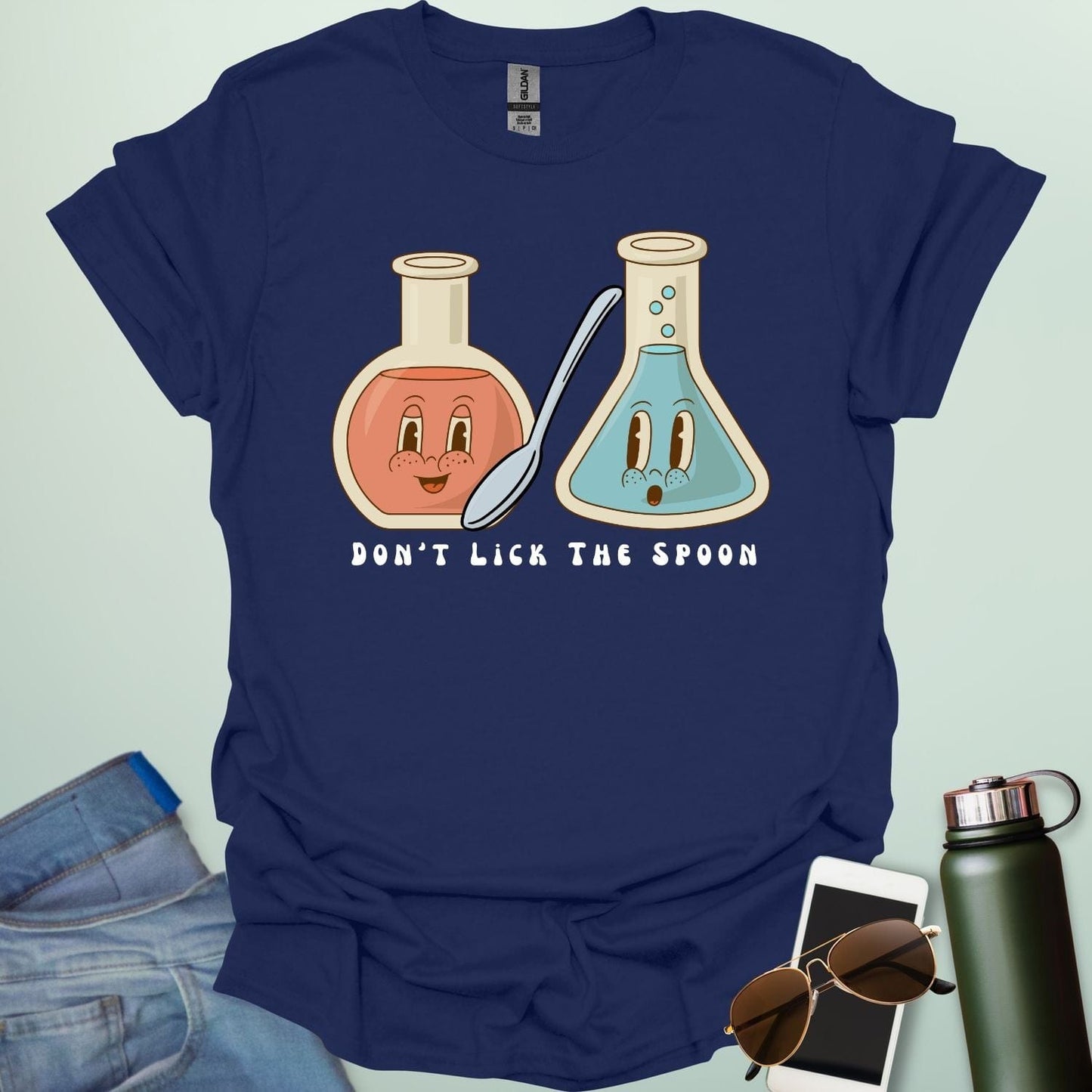 A navy blue t-shirt with a cartoon illustration of two lab flasks and a spoon, with the text 'Don't Lick The Spoon.