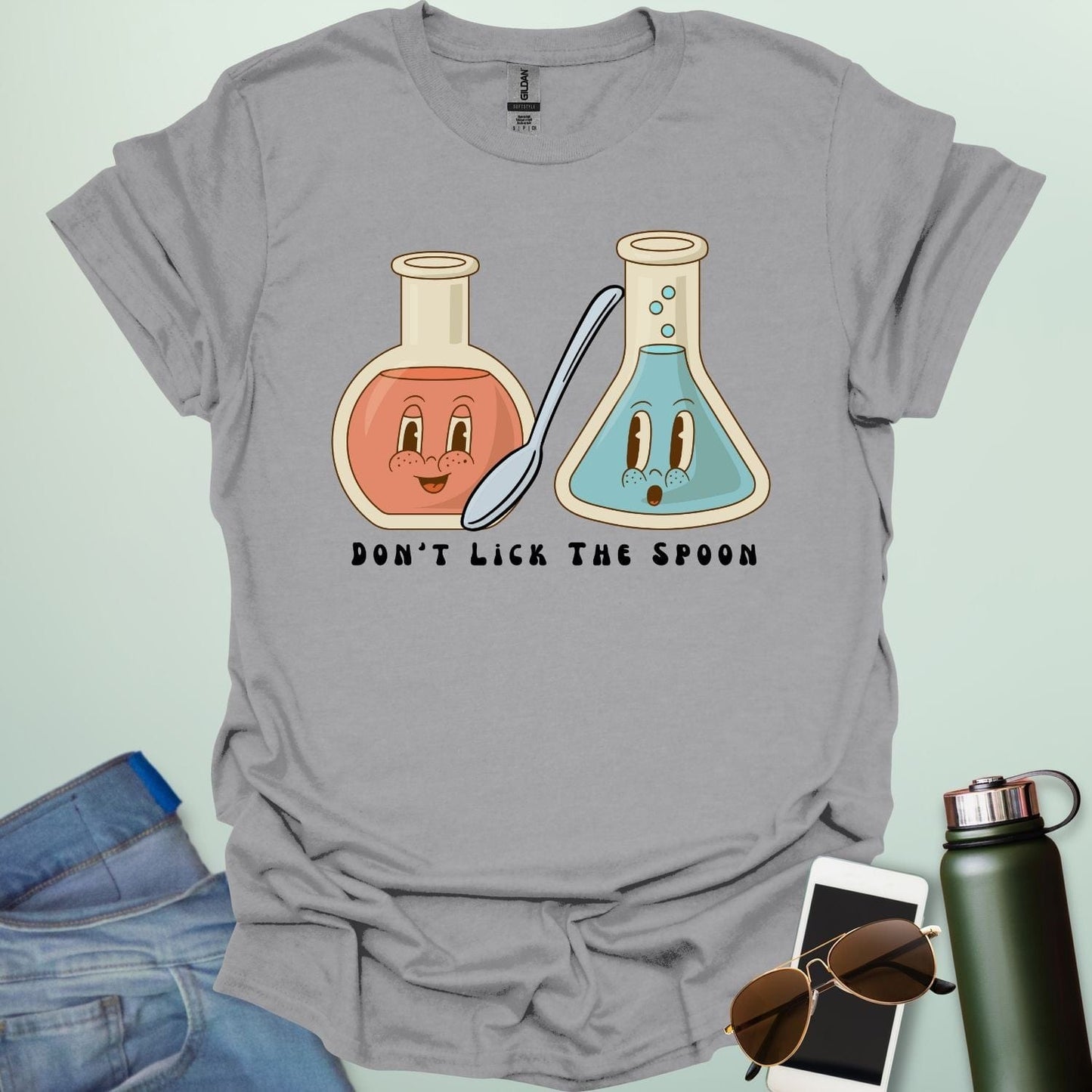A sport grey t-shirt with a cartoon illustration of two lab flasks and a spoon, with the text 'Don't Lick The Spoon.