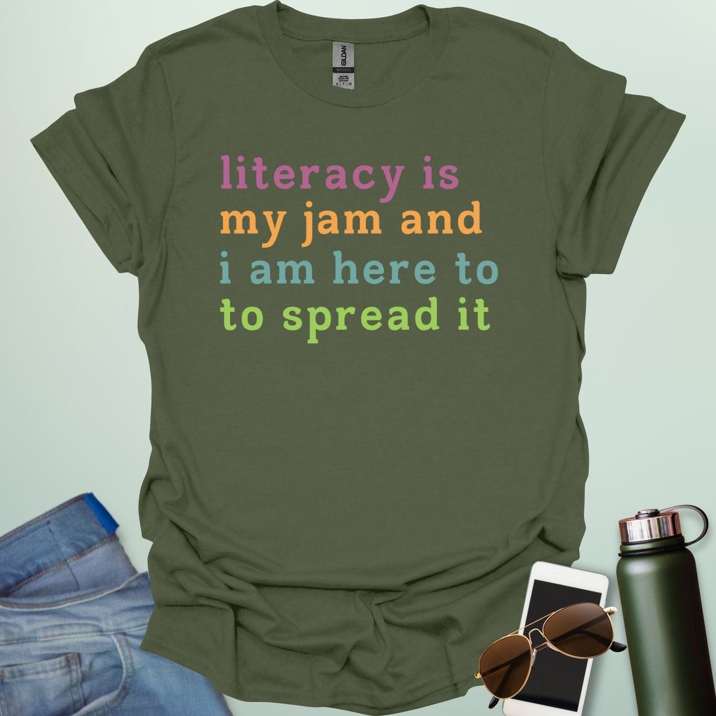 Military green T-shirt with the text 'literacy is my jam and i'm here to spread it' in colorful, bold lettering.