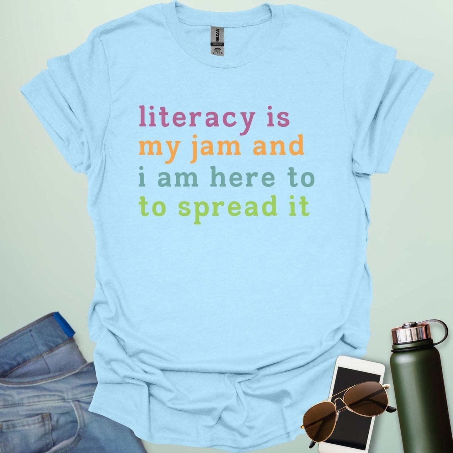 Light blue T-shirt with the text 'literacy is my jam and i'm here to spread it' in colorful, bold lettering.