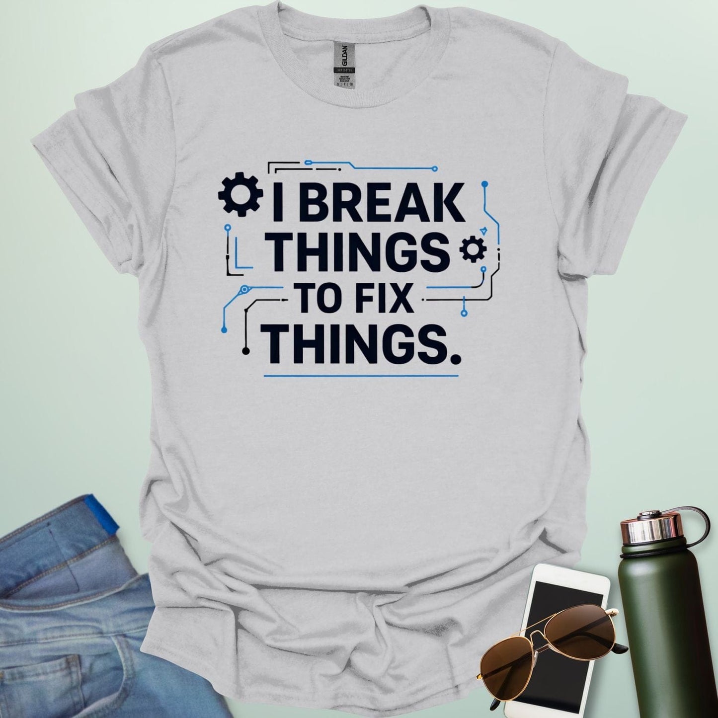 Graphic t-shirt design featuring bold text that reads 'I BREAK THINGS TO FIX THINGS' accented with mechanical gears and electronic circuit board line art.