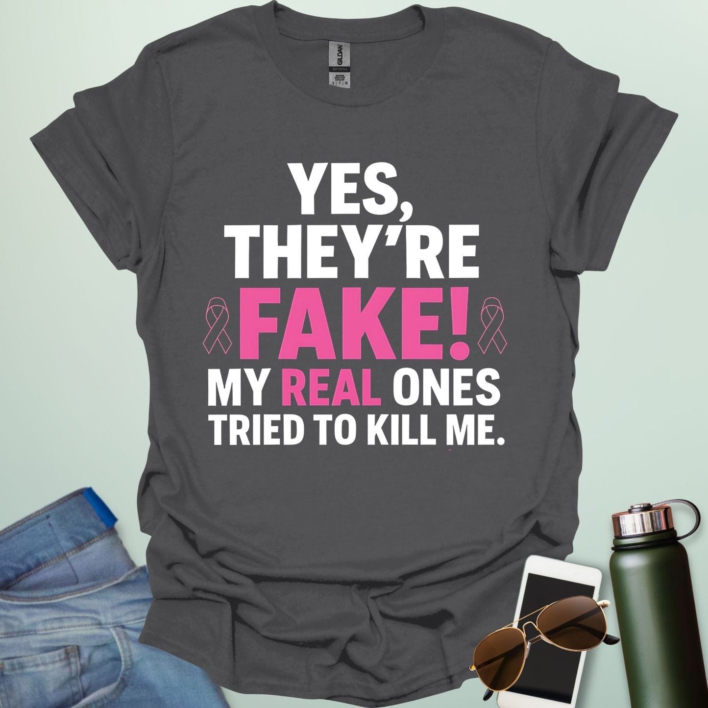 ‘Yes, They’re Fake — My Real Ones Tried to Kill Me’ t-shirt design with bold typography — breast cancer awareness & survivorship statement shirt.