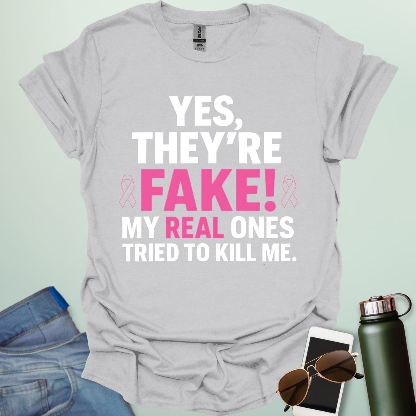 ‘Yes, They’re Fake — My Real Ones Tried to Kill Me’ t-shirt design with bold typography — breast cancer awareness & survivorship statement shirt.