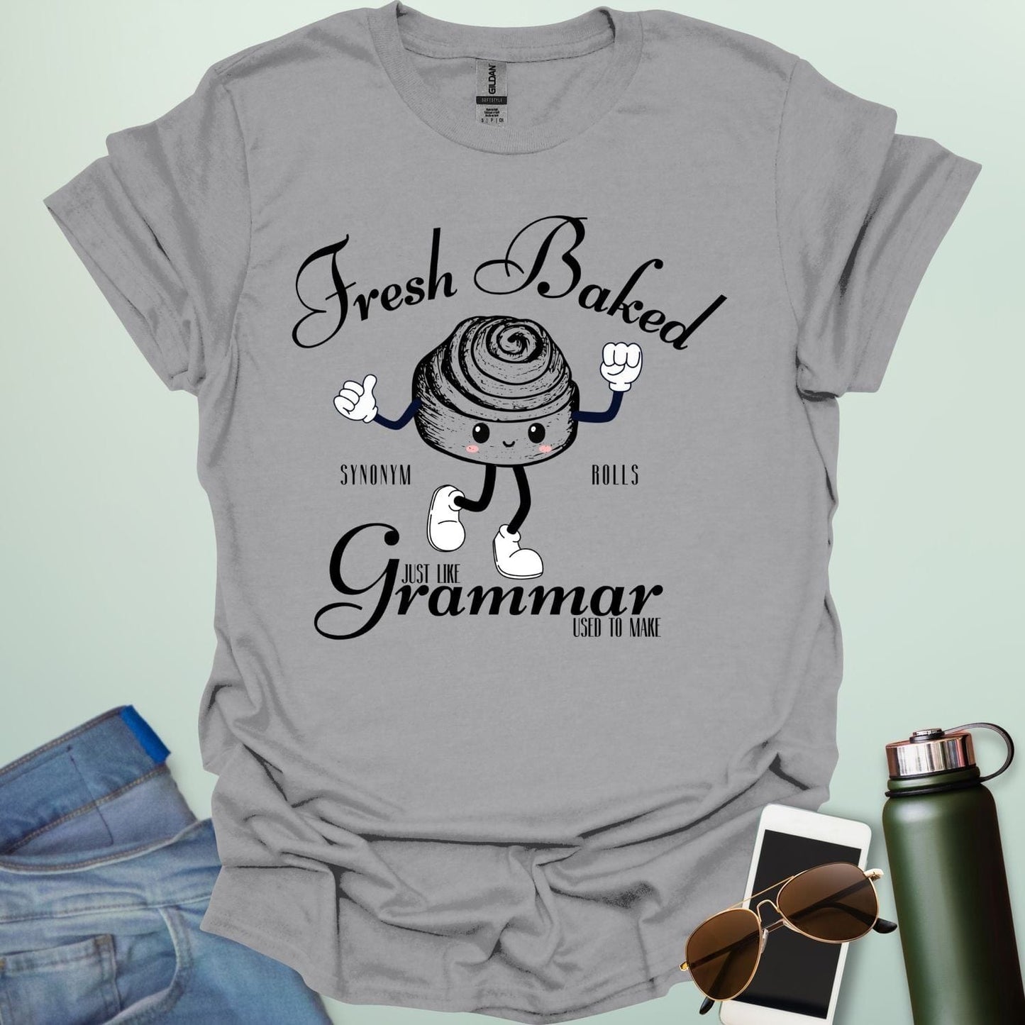 A funny t-shirt with a cute cartoon cinnamon roll and the text 'Fresh Baked Synonym Rolls Just Like Grammar Used to Make.'