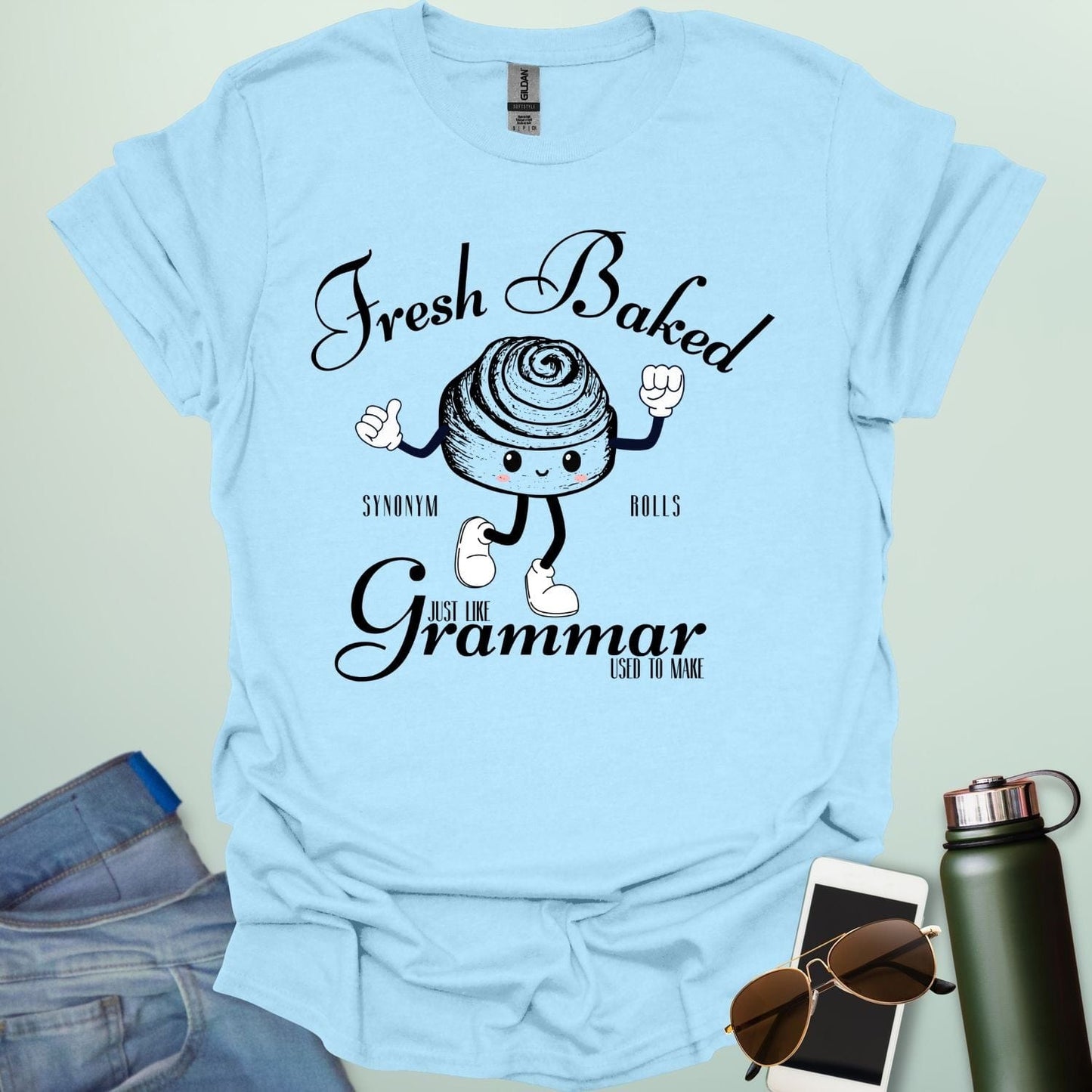 A funny t-shirt with a cute cartoon cinnamon roll and the text 'Fresh Baked Synonym Rolls Just Like Grammar Used to Make.'