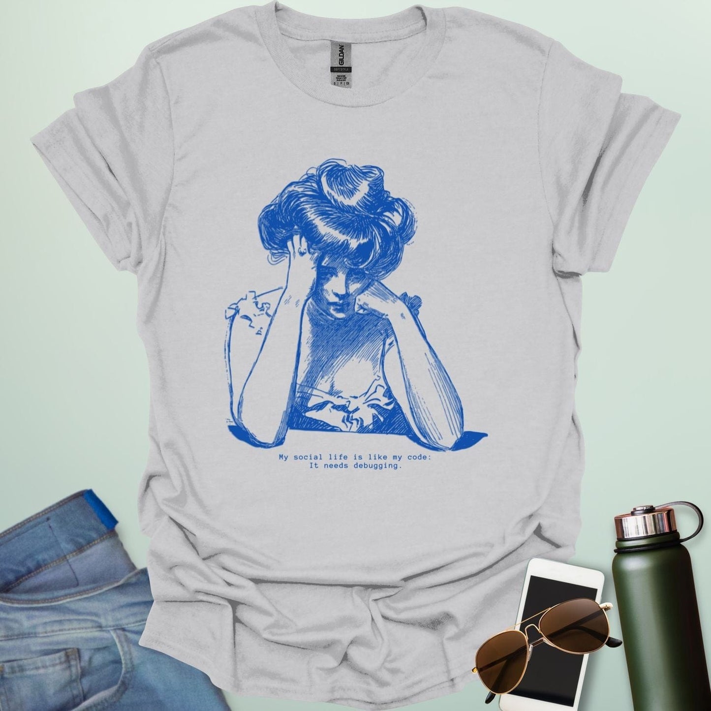 An ice grey shirt with blue line art illustration of a woman looking frustrated with her head in her hands, above the text 'My social life is like my code:' and 'It needs debugging.