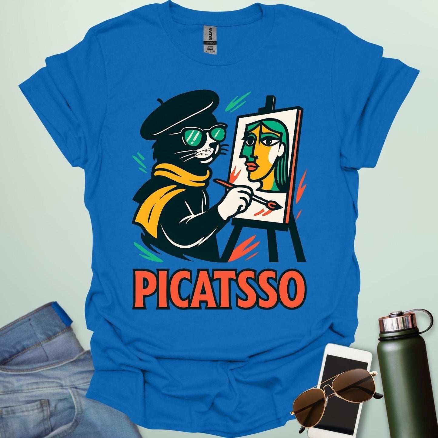 A royal blue t-shirt with a cartoon of a cat painting a Picasso-style portrait on an easel and the text 'PICATSSO' below.