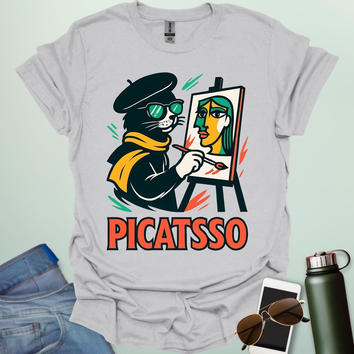 An ice grey t-shirt with a cartoon of a cat painting a Picasso-style portrait on an easel and the text 'PICATSSO' below.