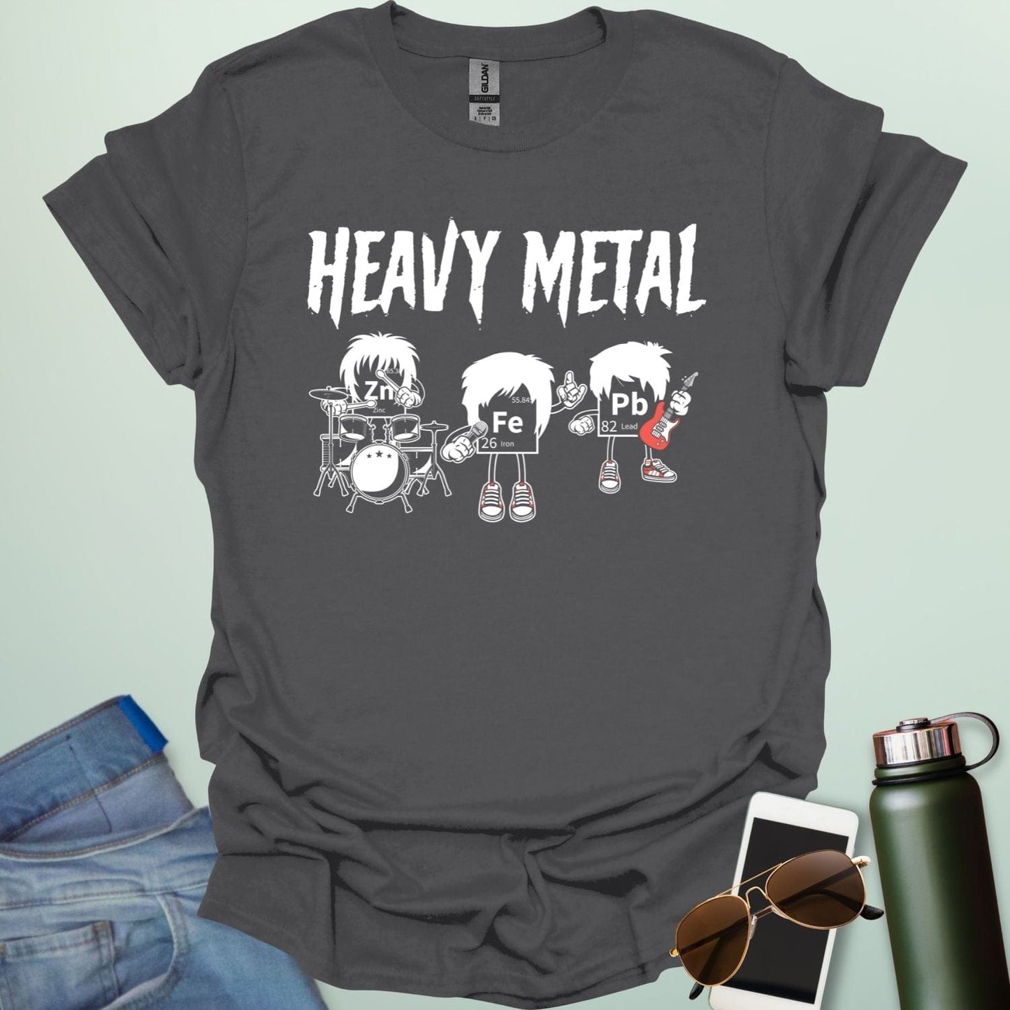 A charcoal grey t-shirt with a cartoon graphic of three chemical elements—Zn, Fe, and Pb—dressed as a heavy metal rock band with the text 'HEAVY METAL' above them.