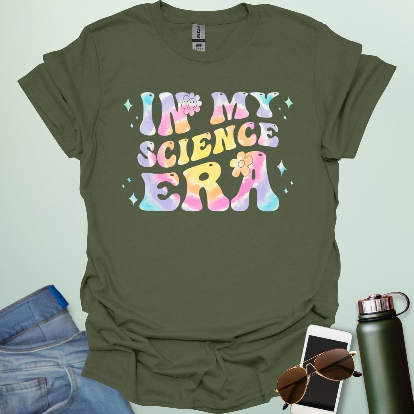 A military green t-shirt with wavy, tie-dye text that says 'IN MY SCIENCE ERA' with flowers and stars.