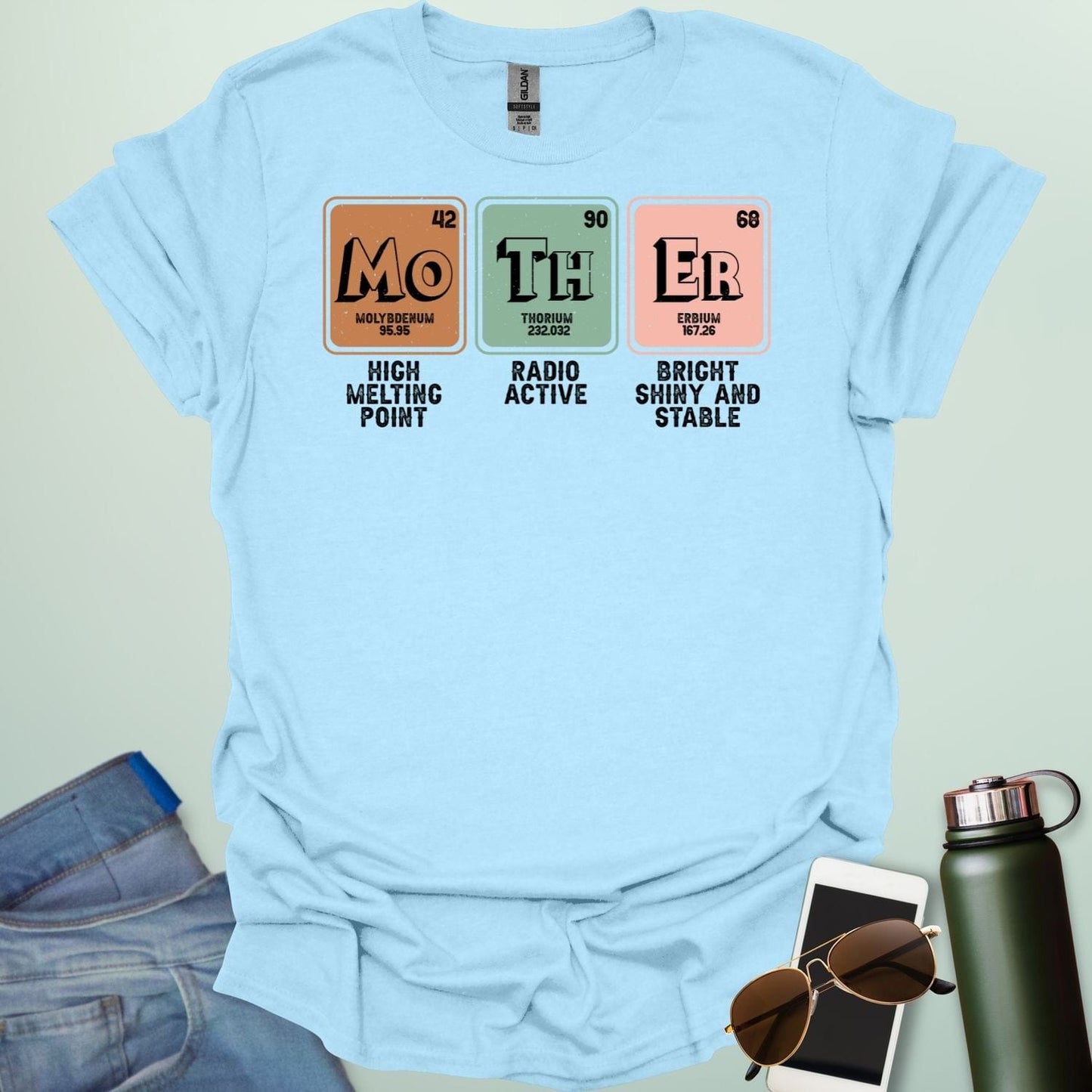 A light blue t-shirt design with three periodic table elements: Mo (Molybdenum), Th (Thorium), and Er (Erbium), with humorous descriptions underneath.