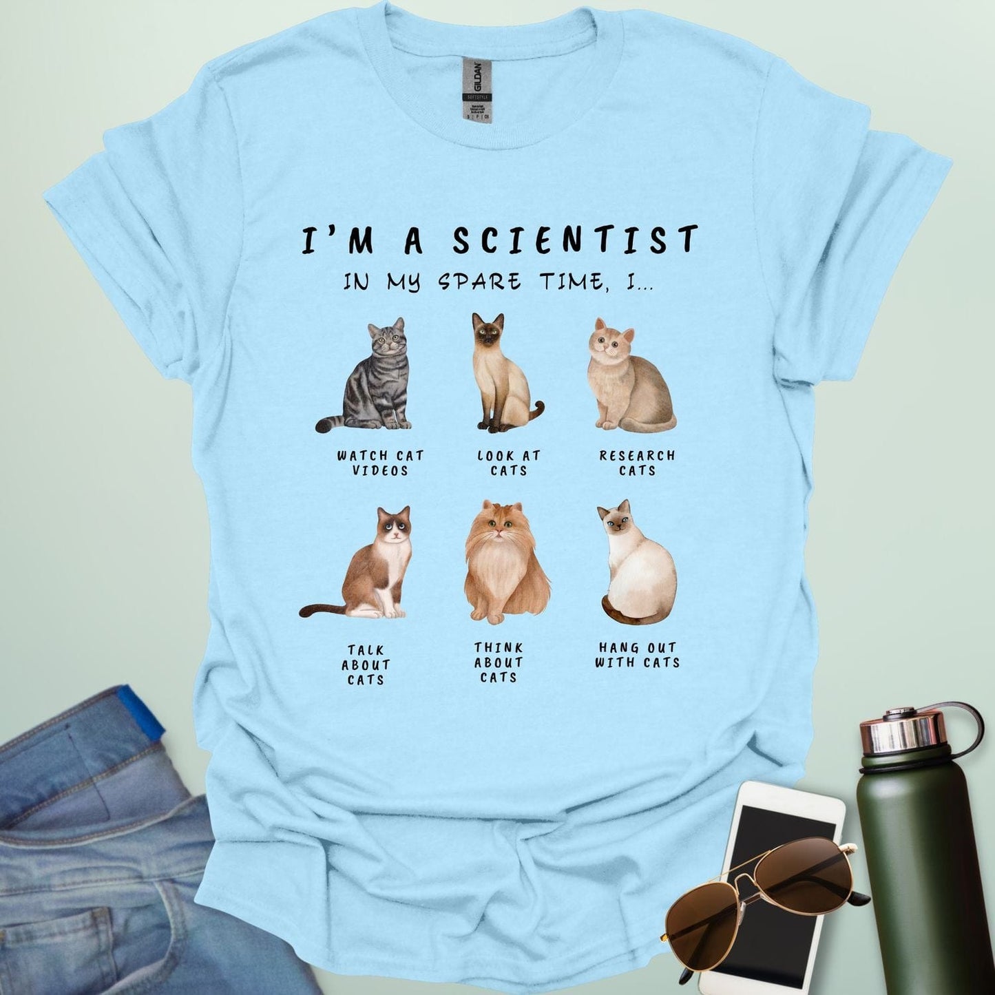 Light blue t-shirt with cat illustrations and text on a light gray background