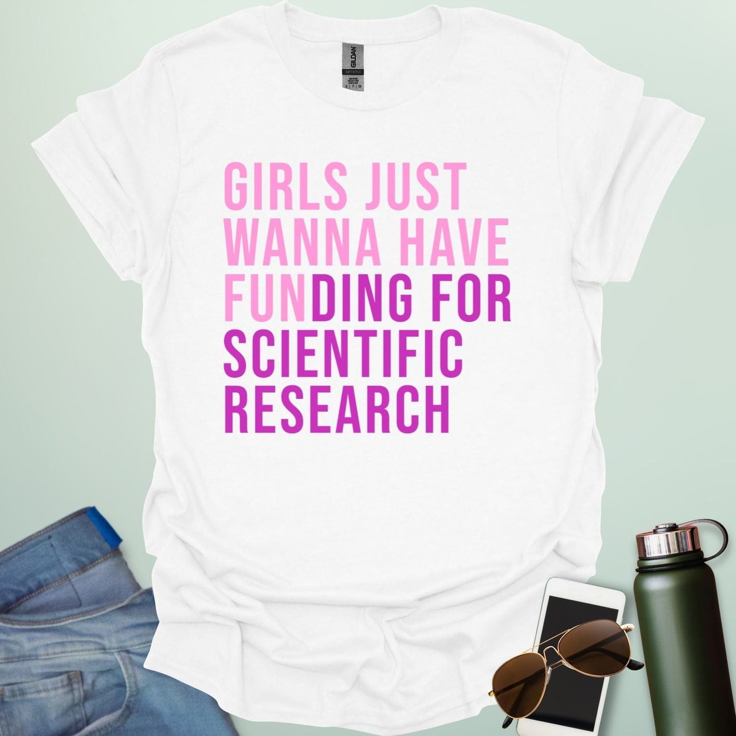 A white t-shirt with the phrase 'Girls just wanna have funding for scientific research' in a bold, pink sans-serif font.