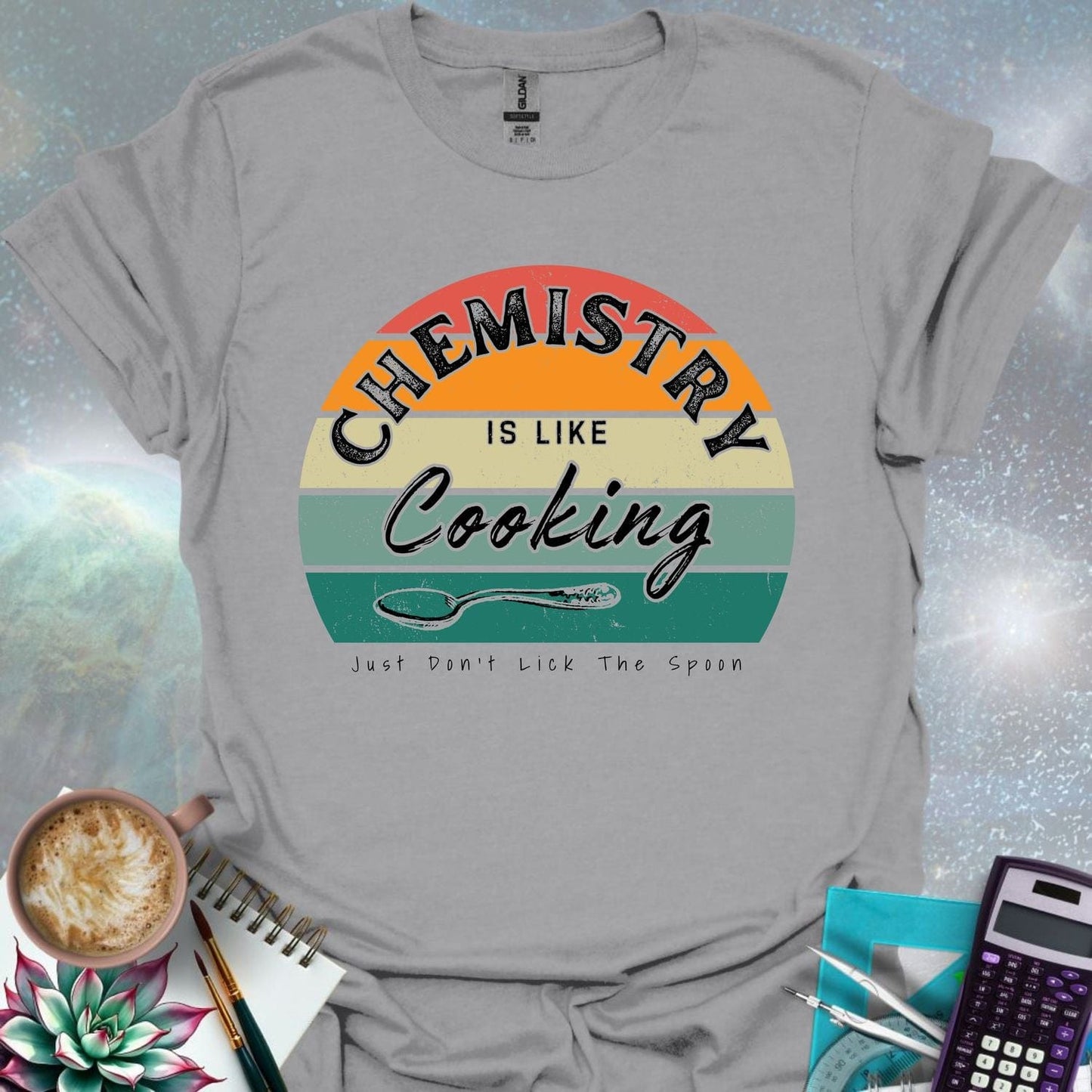 The text 'Chemistry is like Cooking - Just don't lick the spoon' in a distressed, grunge font, with a spoon graphic and a retro-style sunset background.