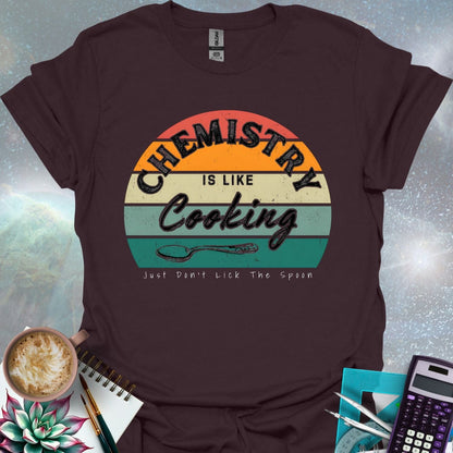 The text 'Chemistry is like Cooking - Just don't lick the spoon' in a distressed, grunge font, with a spoon graphic and a retro-style sunset background.