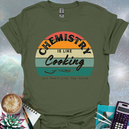 The text 'Chemistry is like Cooking - Just don't lick the spoon' in a distressed, grunge font, with a spoon graphic and a retro-style sunset background.