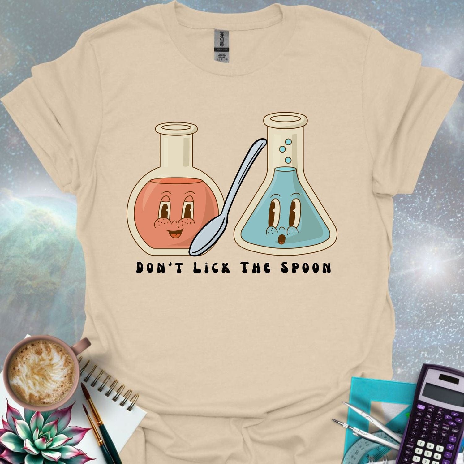 T-shirt design featuring two cartoonish retro beakers, one smiling, one surprised, with a spoon and the text 'Don't Lick The Spoon'.