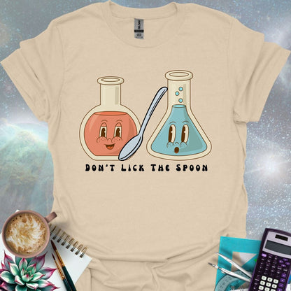 T-shirt design featuring two cartoonish retro beakers, one smiling, one surprised, with a spoon and the text 'Don't Lick The Spoon'.