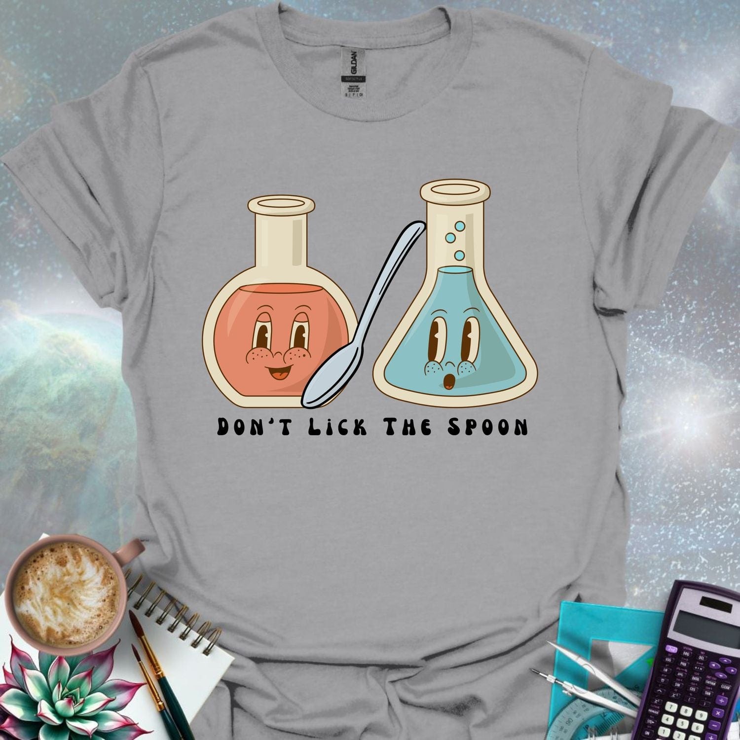 T-shirt design featuring two cartoonish retro beakers, one smiling, one surprised, with a spoon and the text 'Don't Lick The Spoon'.