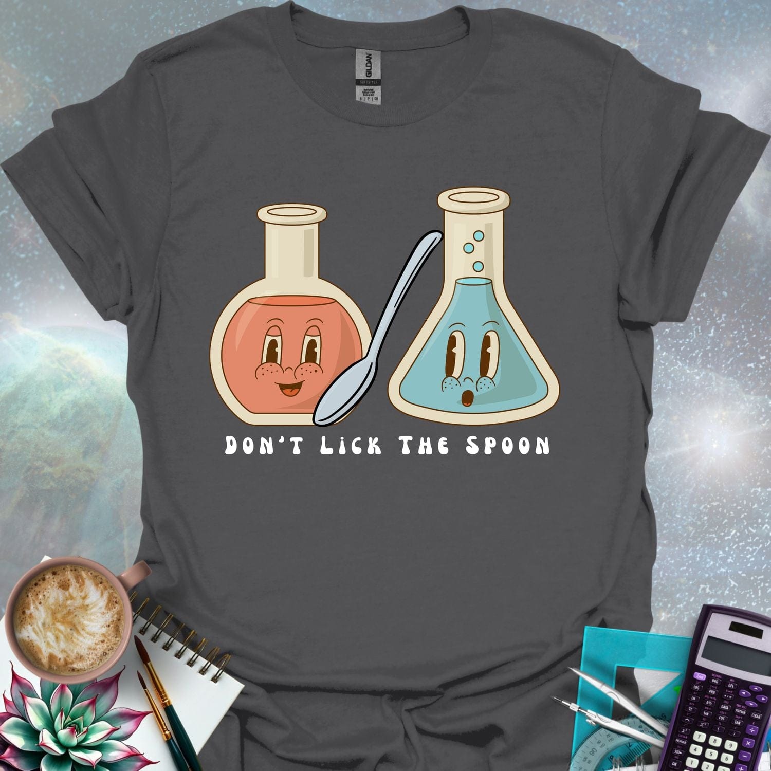 T-shirt design featuring two cartoonish retro beakers, one smiling, one surprised, with a spoon and the text 'Don't Lick The Spoon'.
