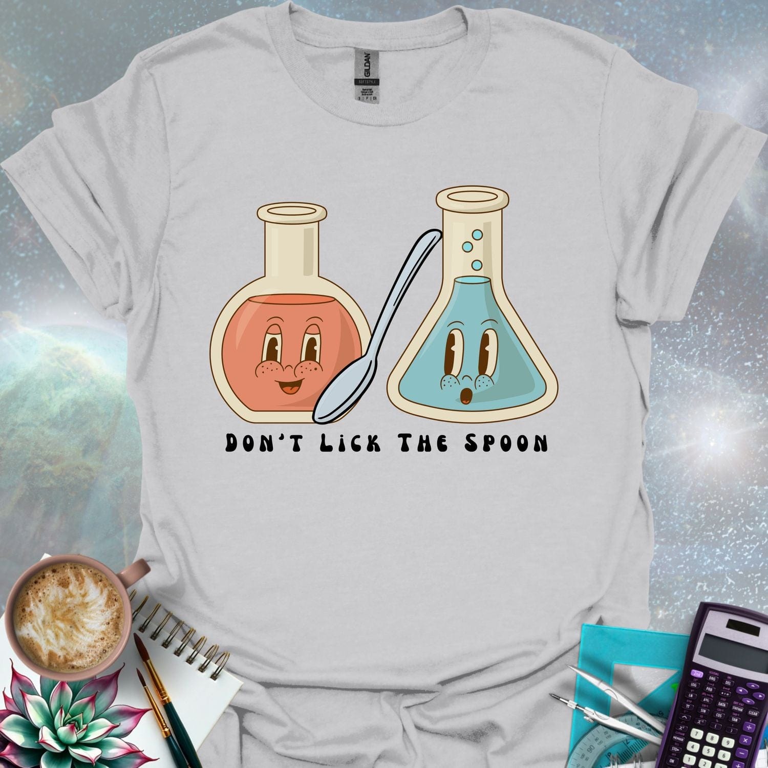 T-shirt design featuring two cartoonish retro beakers, one smiling, one surprised, with a spoon and the text 'Don't Lick The Spoon'.