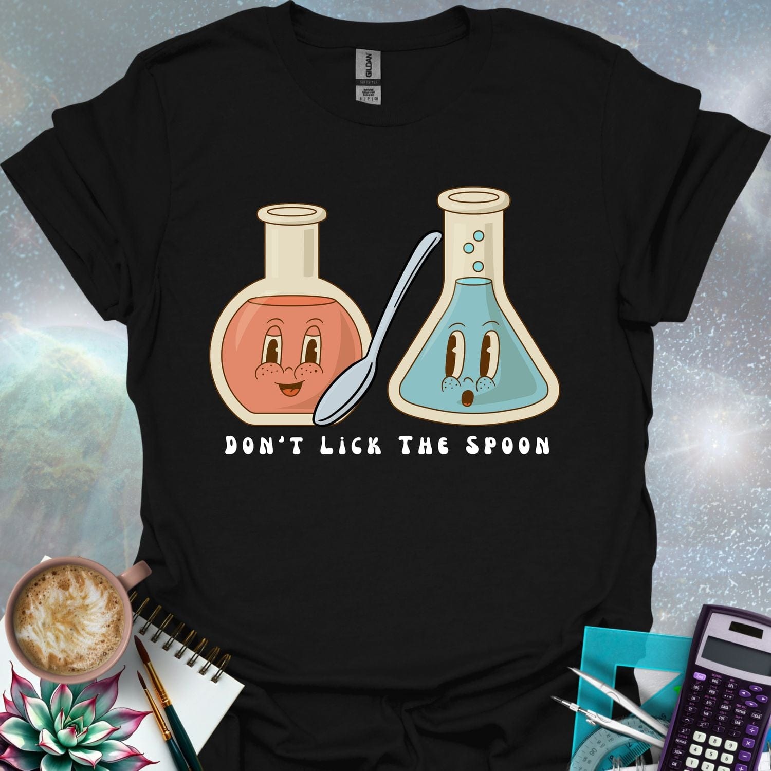 T-shirt design featuring two cartoonish retro beakers, one smiling, one surprised, with a spoon and the text 'Don't Lick The Spoon'.