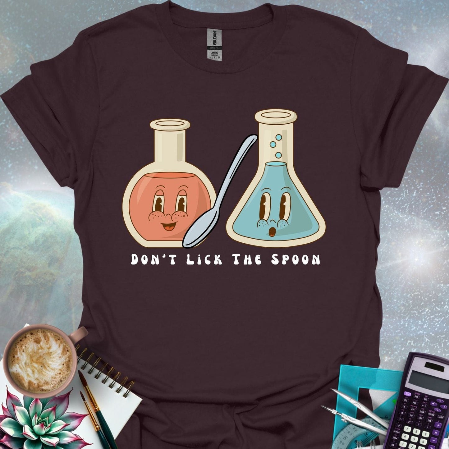T-shirt design featuring two cartoonish retro beakers, one smiling, one surprised, with a spoon and the text 'Don't Lick The Spoon'.