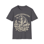 Linocut-style illustration of a bear sitting down examining a stone beside a cairn stack, framed by text reading 'EASILY DISTRACTED BY ROCKS'.