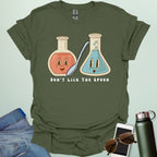 A military green t-shirt with a cartoon illustration of two lab flasks and a spoon, with the text 'Don't Lick The Spoon.