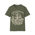 Linocut-style illustration of a bear sitting down examining a stone beside a cairn stack, framed by text reading 'EASILY DISTRACTED BY ROCKS'.