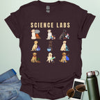 A dark chocolate t-shirt with the text 'SCIENCE LABS' and a grid of nine illustrations of Labrador Retrievers in various science-themed scenarios.