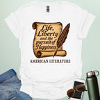 A white t-shirt with a vintage-style scroll and quill pen, and the text 'Life, Liberty and the pursuit of Happiness' and 'American Literature.'