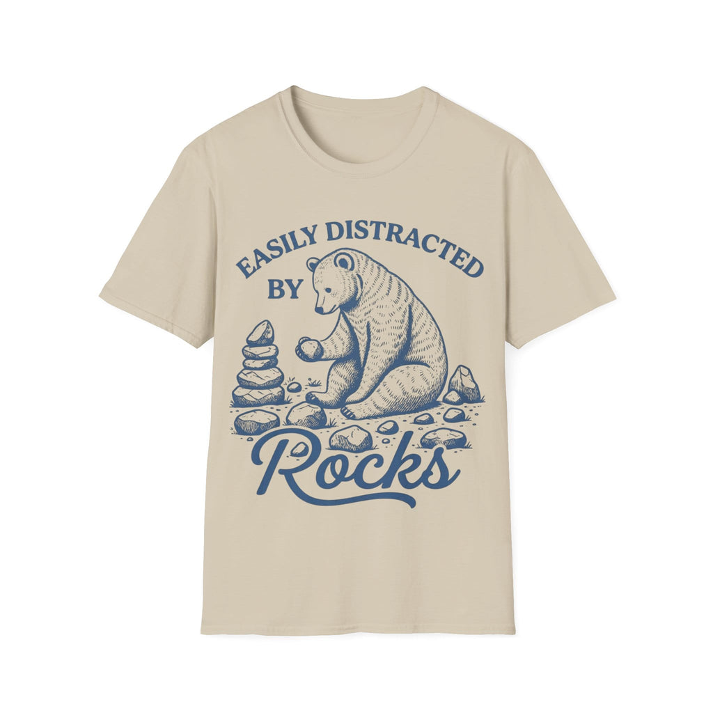 Linocut-style illustration of a bear sitting down examining a stone beside a cairn stack, framed by text reading 'EASILY DISTRACTED BY ROCKS'.
