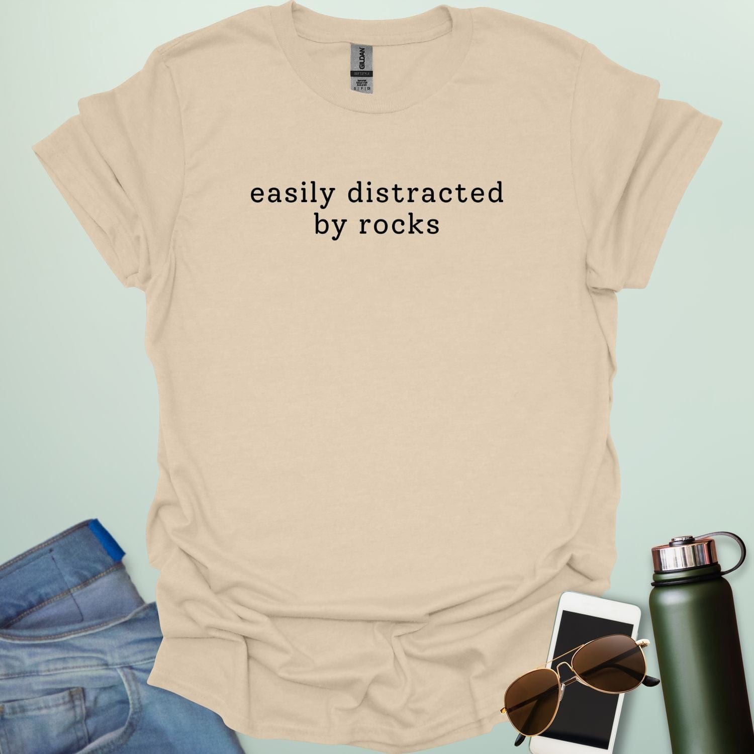 EASYLY DISTRACTED BY ROCKS t-shirt with distressed uppercase typography and small rock icons beside ‘BY’ — minimalist geology humor tee.