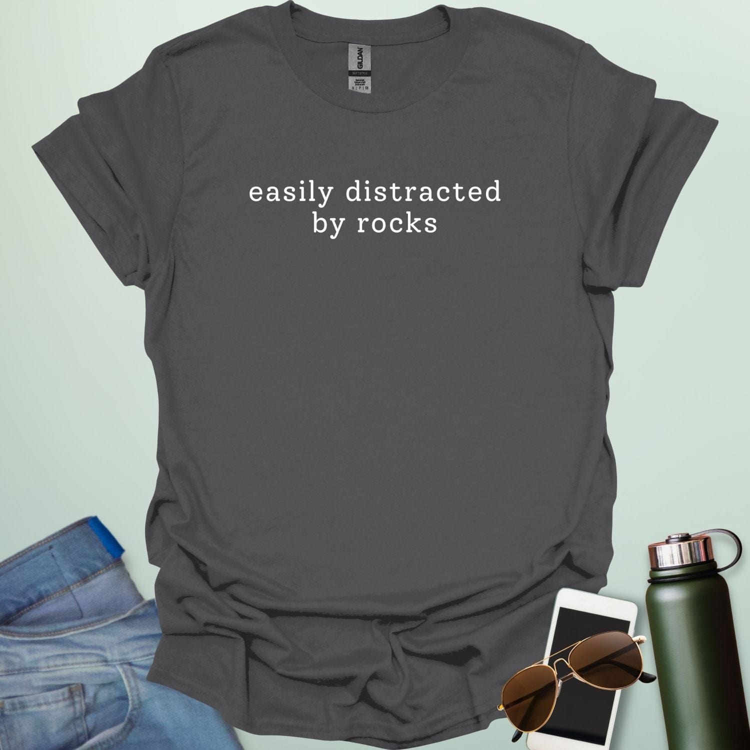 EASYLY DISTRACTED BY ROCKS t-shirt with distressed uppercase typography and small rock icons beside ‘BY’ — minimalist geology humor tee.