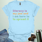 Light blue T-shirt with the text 'literacy is my jam and i'm here to spread it' in colorful, bold lettering.