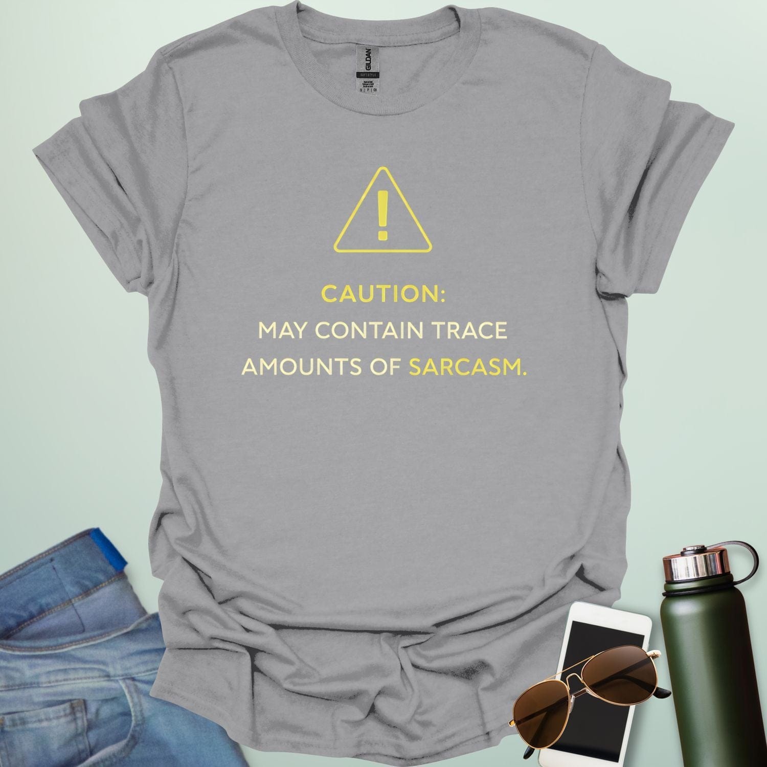A minimalist science-themed design featuring a warning triangle with an "!" in the center with text "CAUTION: MAY CONTAIN TRACE AMOUNTS OF SARCASM" underneath.