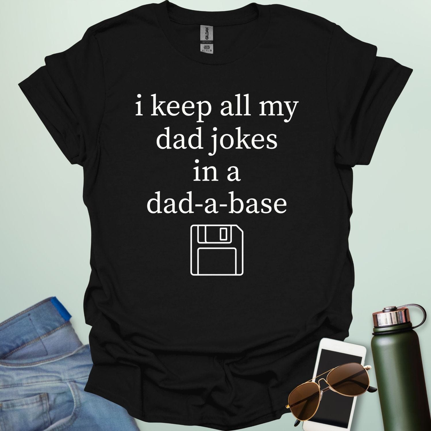 A graphic design featuring white text that reads "i keep all my dad jokes in a dad-a-base" above a minimalist white line art icon of a floppy disk.