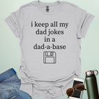 A graphic design featuring white text that reads "i keep all my dad jokes in a dad-a-base" above a minimalist white line art icon of a floppy disk.