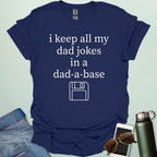 A graphic design featuring white text that reads "i keep all my dad jokes in a dad-a-base" above a minimalist white line art icon of a floppy disk.