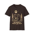 Vintage linocut-style illustration of a bear sitting beside a backpack, gazing up at a full moon over mountains and pine trees with text reading 'THE MOON IS WORTH THE WALK'.