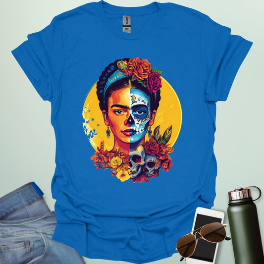 A royal blue t-shirt with a portrait of Frida Kahlo with half of her face as a Dia de los Muertos skull, surrounded by flowers and skulls.