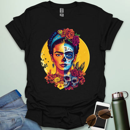 A black t-shirt with a portrait of Frida Kahlo with half of her face as a Dia de los Muertos skull, surrounded by flowers and skulls.