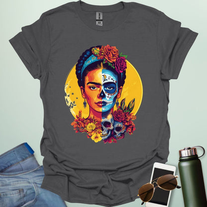 A charcoal grey t-shirt with a portrait of Frida Kahlo with half of her face as a Dia de los Muertos skull, surrounded by flowers and skulls.