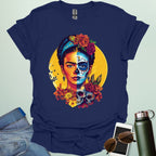 A navy blue t-shirt with a portrait of Frida Kahlo with half of her face as a Dia de los Muertos skull, surrounded by flowers and skulls.