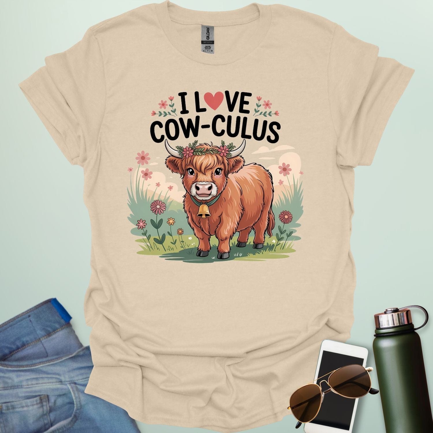 A sand color t-shirt with a cute illustration of a cow in a field and the text 'I love Cow-culus' with a heart symbol.