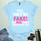 ‘Yes, They’re Fake — My Real Ones Tried to Kill Me’ t-shirt design with bold typography — breast cancer awareness & survivorship statement shirt.
