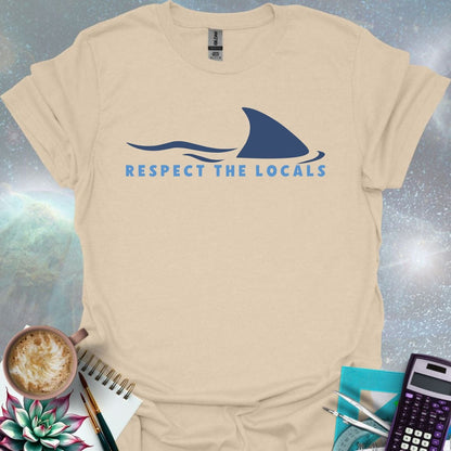 A blue shark fin rising above blue ocean waves, with the text 'RESPECT THE LOCALS' below.